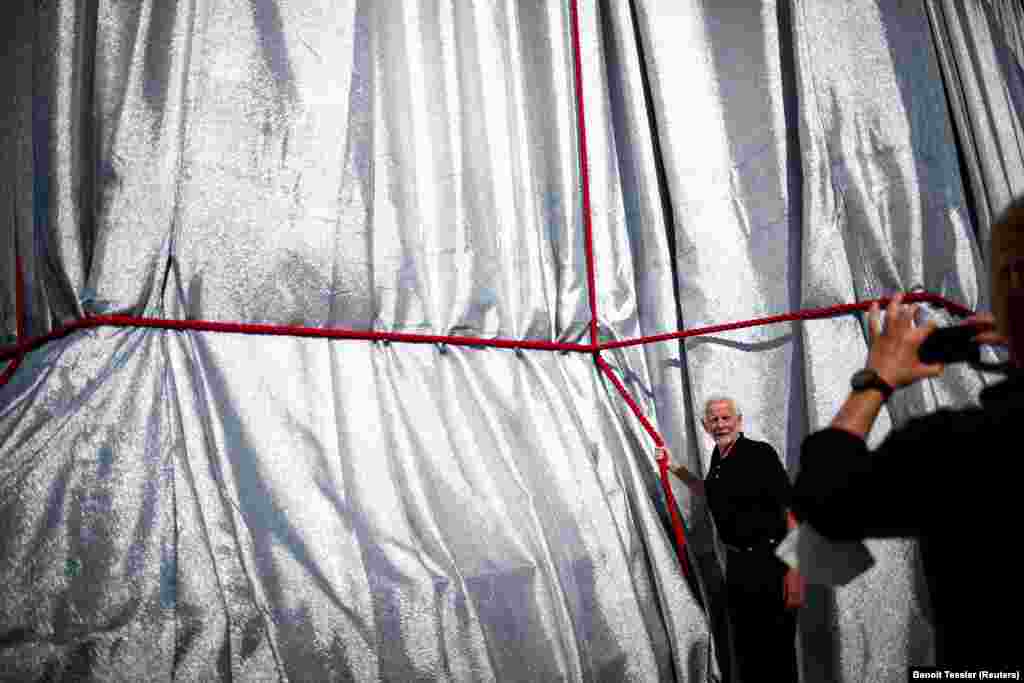 A man poses for a picture alongside the wrapped base of the arch. The red, silver, and blue of the installation was an homage to the French flag. &nbsp;