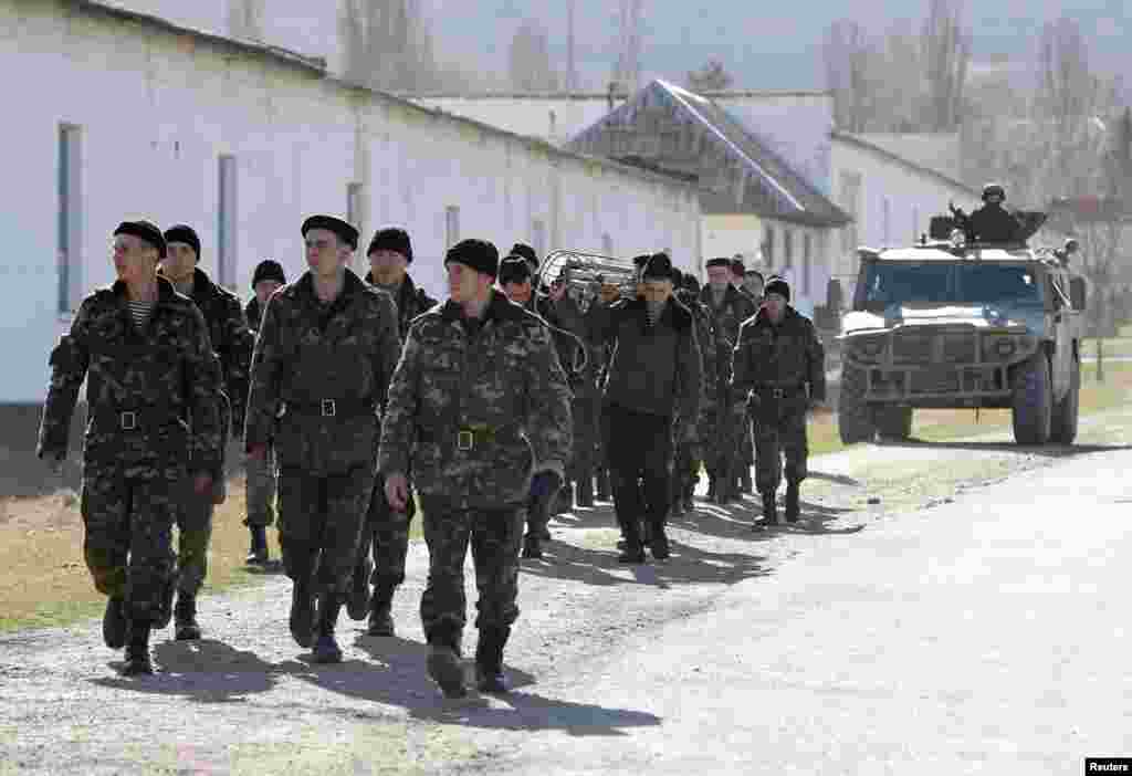 Ukrainian servicemen walk near Simferopol as a military vehicle, believed to be property of the Russian army, follows behind them.