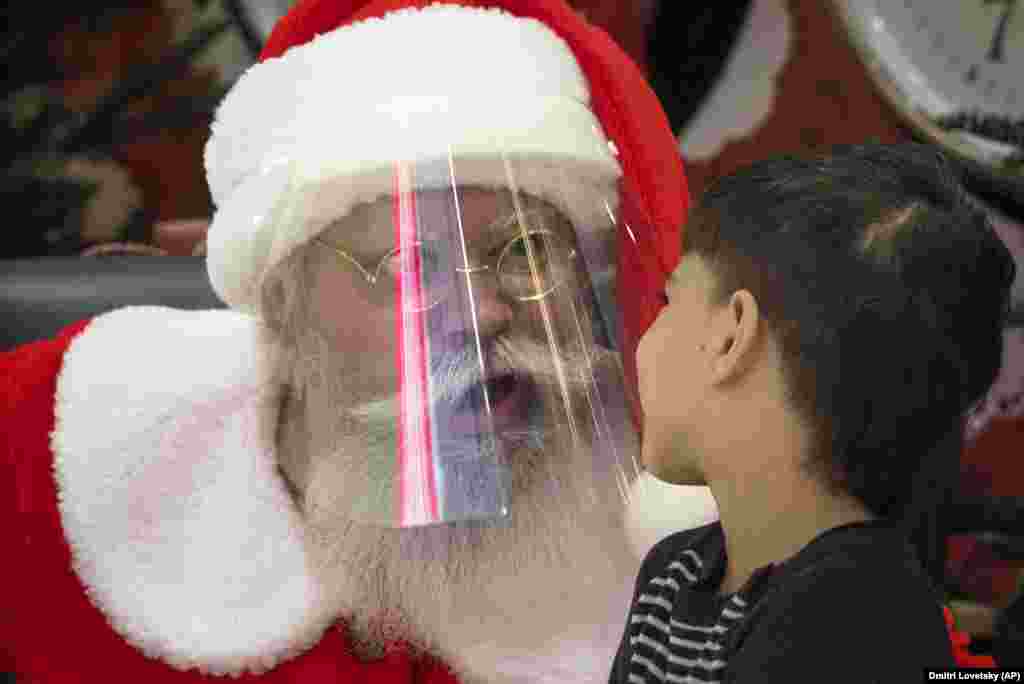 An actor dressed as Santa Claus and wearing a face mask to protect against the coronavirus speaks with a boy in a shopping mall in St. Petersburg, Russia. (AFP/Dmitri Lovetsky)