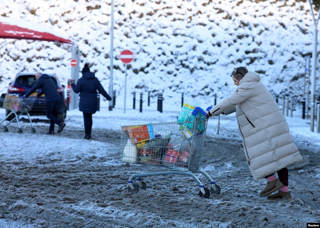 Një grua shtyn një karrocë pazari në borë, teksa Zyra Meteorologjike e Britanisë i zgjati paralajmërimet për mot shumë të ftohtë dhe me akull në Ballimena, Irlanda e Veriut, më 5 janar 2026.