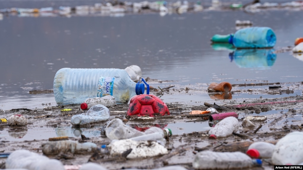 Në mesin e mbeturinave në brigjet e liqenit, shihet edhe një top i shfryrë e shishe uji.