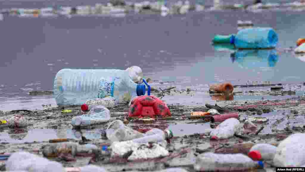 Në mesin e mbeturinave në brigjet e liqenit, shihet edhe një top i shfryrë e shishe uji.