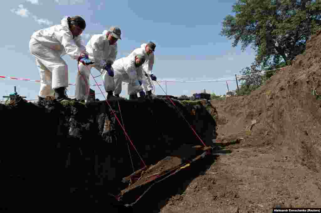 Volunteers lift a coffin from a mass grave during the exhumation of the remains of civilians and military personnel killed during the conflict in Ukraine, in the separatist-controlled village of Snizhne in the Donetsk region.&nbsp;