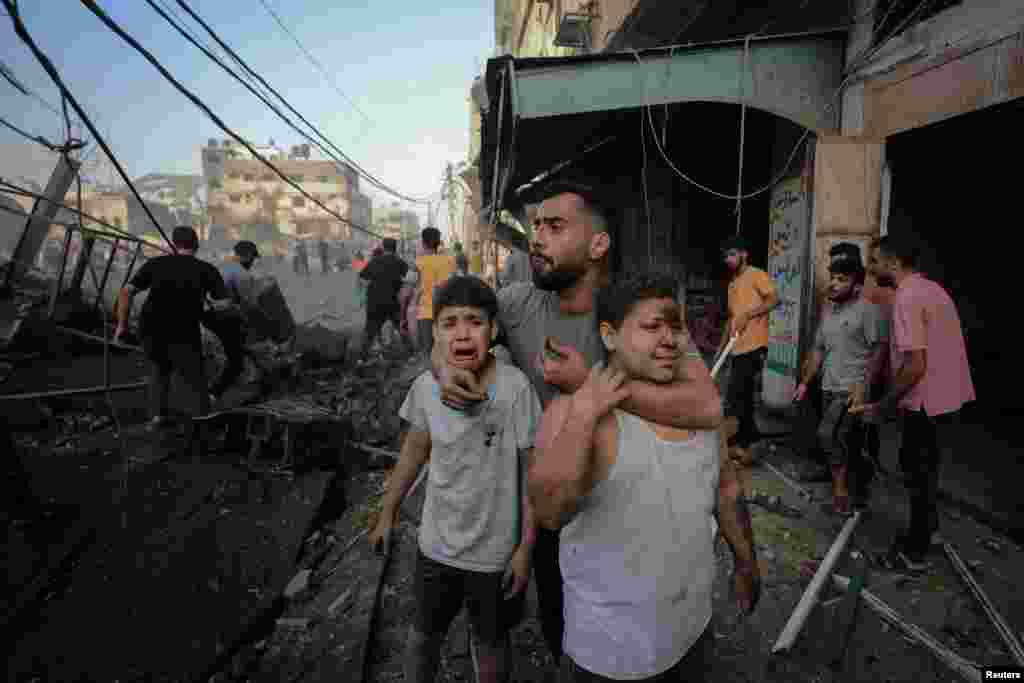 Një burrë përpiqet t&#39;i qetësojë dy fëmijë që po qajnë ndërsa të tjerë palestinezë kërkojnë për viktima në vendin e sulmeve izraelite në një ndërtesë banimi në qytetin e Gazës, 25 tetor 2023.