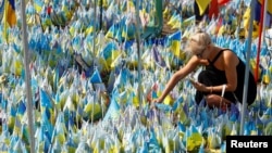 A woman installs a national flag with the name of her husband at a makeshift memorial for fallen Ukrainian soldiers on the Day of Remembrance for Ukraine's Defenders in Kyiv on August 29.