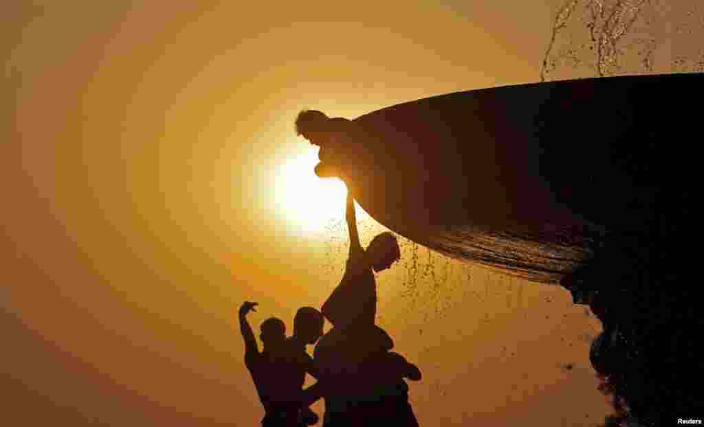 Boys cool off under a water fountain on a hot summer evening in New Delhi, India. (Reuters/Anindito Mukherjee)