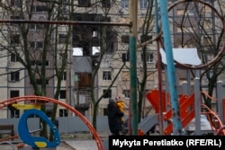 A mother with her child at a children's playground in Dnipro looks at a building damaged by a Russian attack in November, December 11.