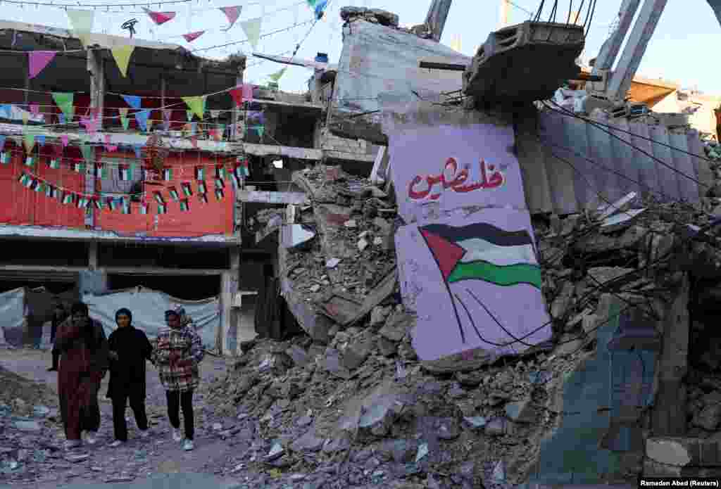 Palestinezët kalojnë pranë një grafiti dhe rrënojave të ndërtesave në Han Junis, teksa bëhen gati për agjërim.&nbsp;