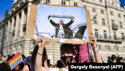 Tüntető plakáttal, rajta Orbán Viktor magyar miniszterelnök egy szivárványszínű sállal a kezében. A kép Budapesten, a Parlament épülete előtt, a magyar kormánynak a homoszexualitás és a nemváltoztatás „népszerűsítését” betiltani kívánó törvénytervezete elleni tüntetésen készült 2021. június 14-én