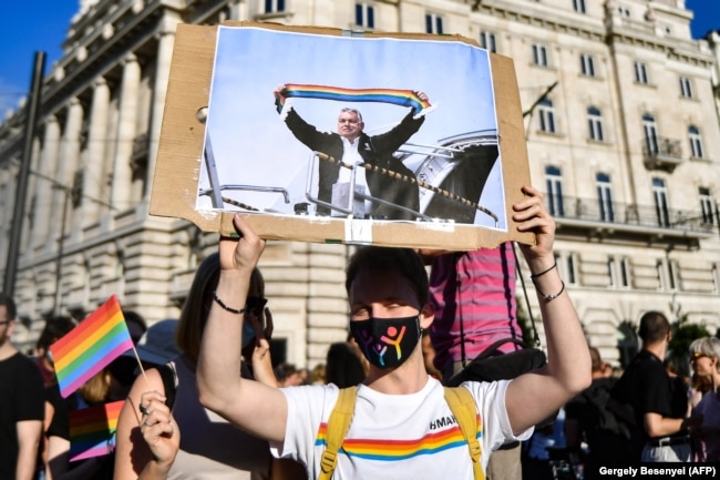 Një protestues duke e mbajtur një pankartë që e shfaq kryeministrin e Hungarisë, Viktor Orban, duke e mbajtur një shall me ngjyrat e ylberit, pranë ndërtesës së Parlamentit në Budapest, gjatë një proteste më 14 qershor 2021.
