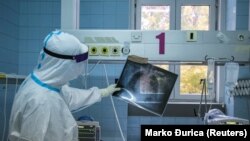 Медработник в защитной одежде изучает рентген-снимок пациента с COVID-19 в клинике в Белграде, столице Сербии. Иллюстративное фото.