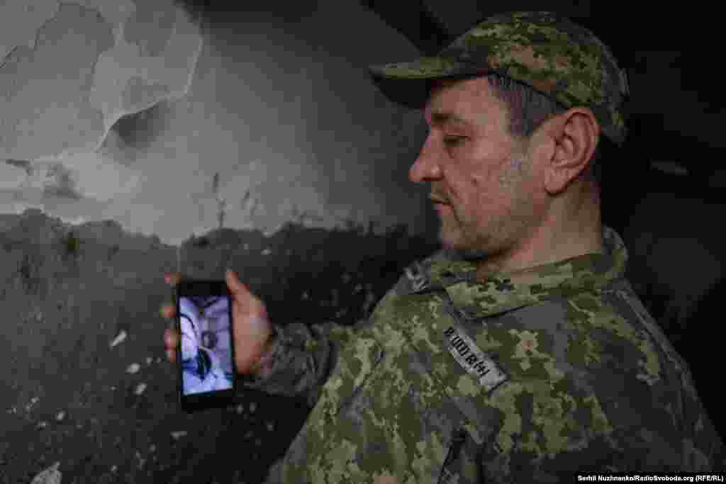 У грудні 2024 року бійці 8-го окремого гірсько-штурмового батальйону 10-ї ОГШБ тримали передові позиції у Дворічній, на Харківщині. Вже за два дні російські сили перерізали українським бійцям логістику. Ці чоловіки опинилися в повному оточенні, але продовжували тримати свої позиції. Вони оборонялися 92 дні. Роман із побратимом ‒ єдині з усієї групи, хто вийшов звідти. Через засилля FPV-дронів ротація стає однією із найнебезпечних задач і основні втрати підрозділи несуть саме під час ротацій. Тому військові змушені залишатися на позиціях тижнями і місяцями, а все необхідне їм скидають вантажні дрони чи привозять НРК. На фото – Роман, піхотинець 8-го окремого гірського-штурмового батальйону 10-ї ОГШБ показує на телефоні побут під час перебування в оточенні, де він пробув із побратимами 92 дні. Харківська область, 1 квітня 2025 року