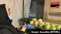 Клиент овощного ларька записывает телефонный номер продавца, чтобы оплатить покупки. Номер указан на стене. Алматы, 25 февраля 2021 года.