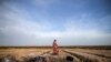 A migrant uses a blanket to warm himself in a field near Edirne, at the Turkish-Greek border on Tuesday, March 3, 2020. Migrants and refugees hoping to enter Greece from Turkey appeared to be fanning out across a broader swathe of the roughly 200-kilomete