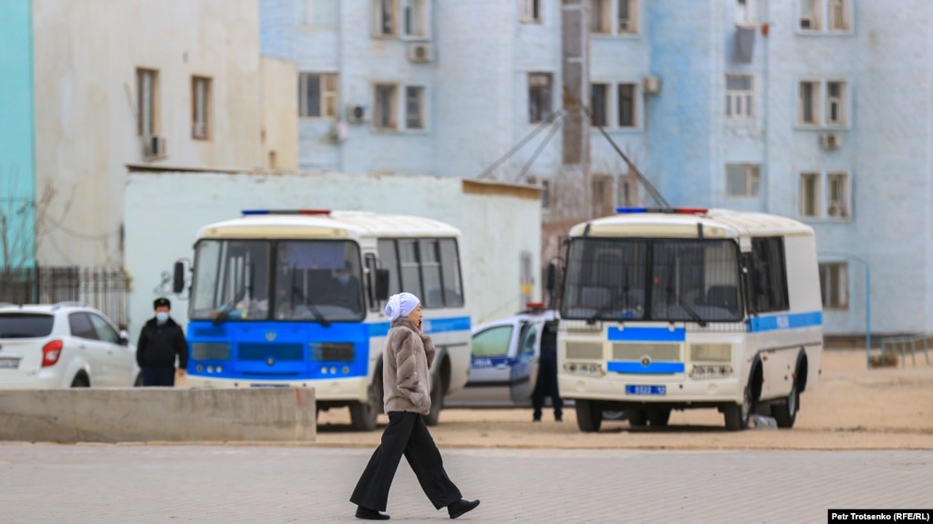 Прохожая идет на фоне полицейских автобусов в городе Жанаозене