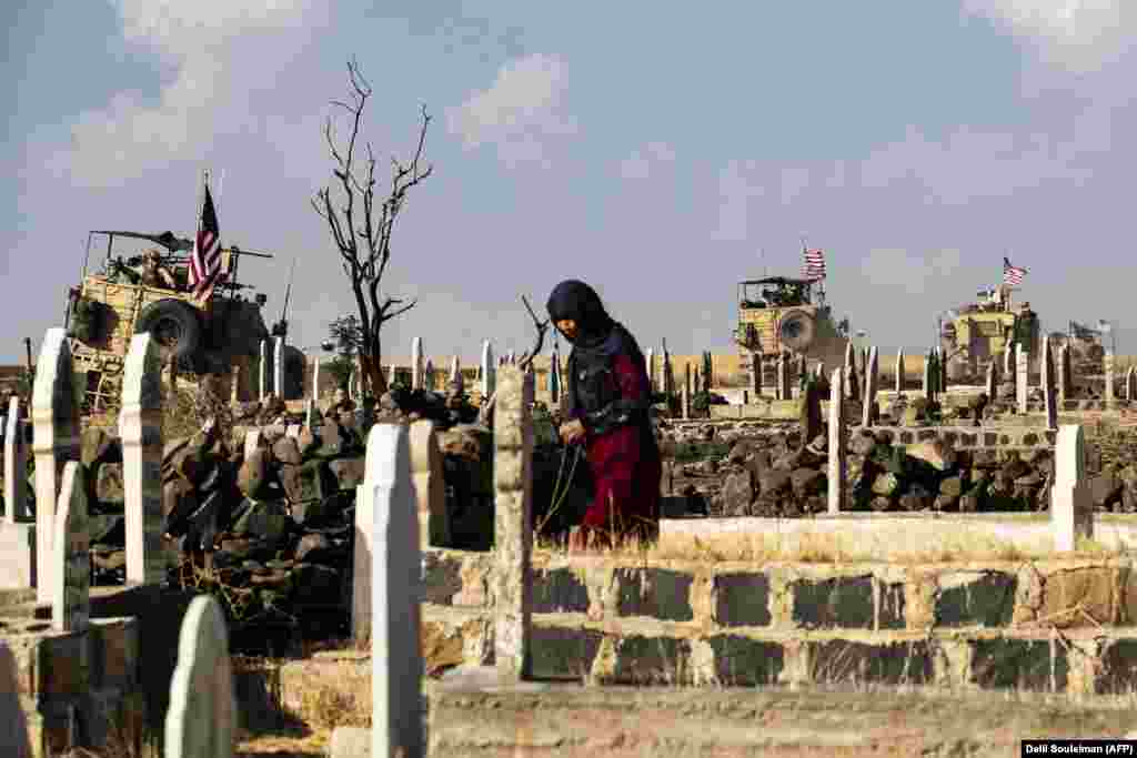 A Syrian woman visits a cemetery as U.S. armored vehicles patrol the northeastern town of Qahtaniyah near the border with Turkey. (AFP/Delil Souleiman)