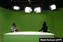 A female news presenter with her face covered by a veil speaks with a guest in a Kabul studio in May 2022.