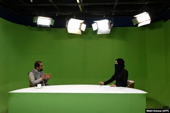 Një prezantuese e lajmeve, me fytyrën e mbuluar, flet me një të ftuar në një studio në Kabul në maj 2022.