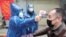 A worker takes body temperature measurement of a man at the entrance to a residential compound following an outbreak of the new coronavirus in Wuhan, Hubei province, February 1, 2020