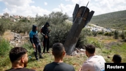 People gather around remnants of a missile stuck in the ground found in Kifl Haris village, near Nablus in the Israeli-occupied West Bank, on March 24.