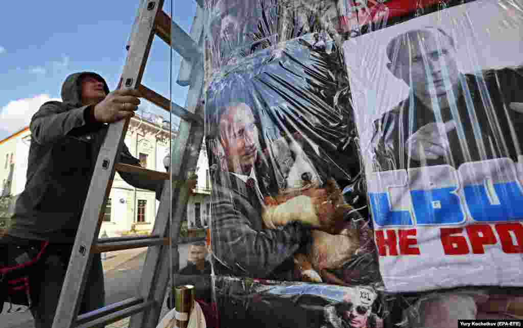 A man climbs a ladder near a Moscow storefront with T-shirts displaying portraits of Russian President Vladimir Putin. (epa-EFE/Yuri Kochetkov)