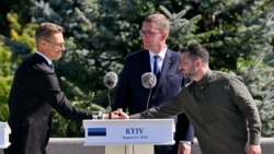 ფინეთის პრეზიდენტი ალექსანდრ სტუბი ხელს ართმევს უკრაინის პრეზიდენტ ვოლოდიმირ ზელენსკის უკრაინის სახელმწიფო დროშის დღისადმი მიძღვნილ ცერემონიაზე. შუაში  ესტონეთის პრემიერმინისტრი კრისტენ მიხალი. კიევი, 2026 წლის 23 აგვისტო
