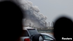 Oameni privind nori de fum deasupra rafinăriei Bapco de pe insula Sitra din Bahrain, pe 9 martie 2026