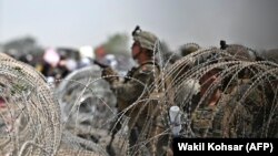 Soldații americani stau de pază în spatele sârmei ghimpate în timp ce afganii se adună pe marginea drumului lângă partea militară a aeroportului din Kabul, 20 august 2021