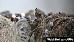 Американски војници чуваат стража зад бодликава жица додека Авганистанцит се собираат на пат во близина на воениот дел на аеродромот во Кабул. 20 август 2021 година