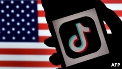 Logoja e TikTok-ut në ekranin e një telefoni mobil, me flamurin amerikan në prapavijë. Fotografi ilustruese.