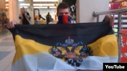 A masked young man holds up a CSKA banner at the end of the YouTube video in question.