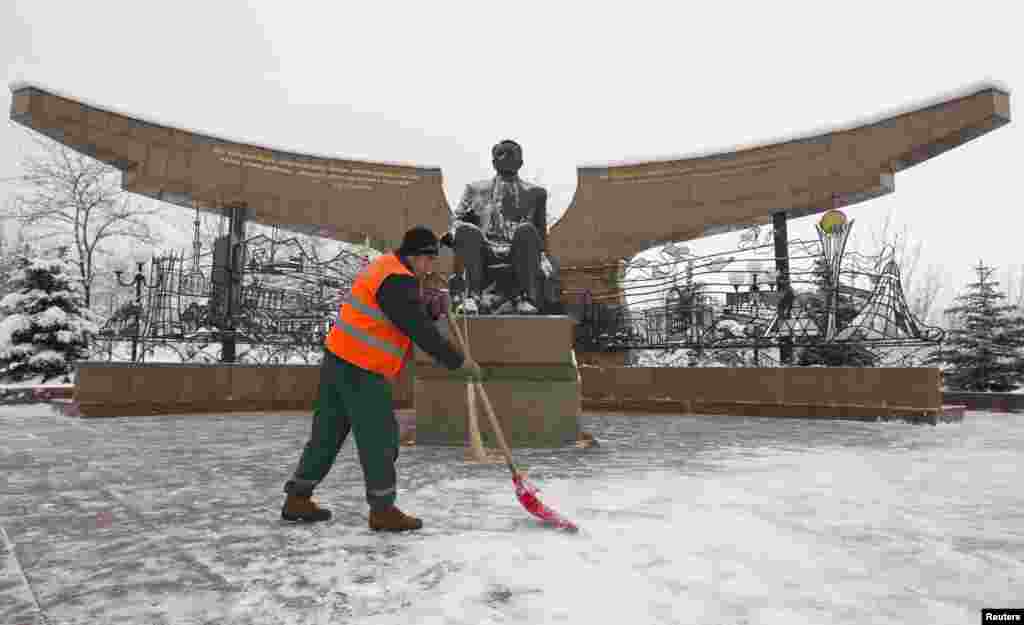 A worker removes snow in front of a statue of President Nursultan Nazarbaev at the Park of the First President on the eve of the Day of the First President in Almaty.