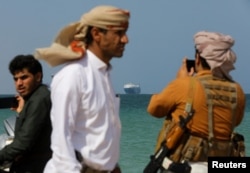 Люди на берегу Красного моря на фоне грузового судна Galaxy Leader, захваченного хуситами у берегов Йемена в декабре 2023 года