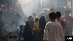 An Afghan burqa-clad woman carries a child on a busy market street in Mazar-i Sharif.