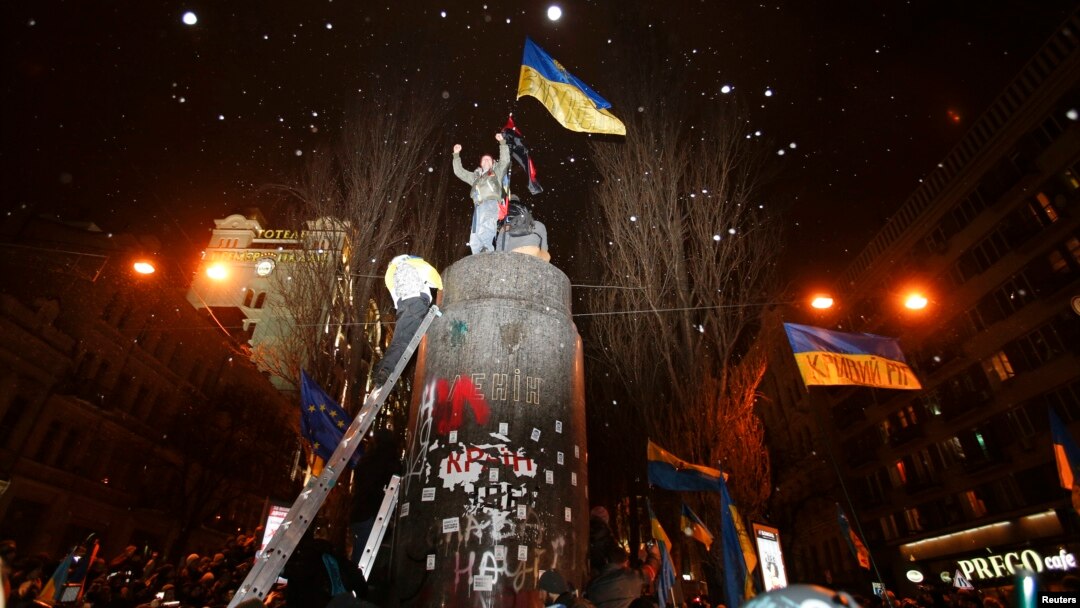 People climb atop the pedestal where a statue of Soviet state founder Vladimir Lenin was toppled earlier on December 8 after a rally organized by supporters of EU integration in Kyiv.