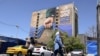 People cross a street near a billboard on the facade of a building depicting the Strait of Hormuz with a caption in Persian reading "Forever in Iran’s Hand", at Vanak Square in Tehran on May 25, 2026.