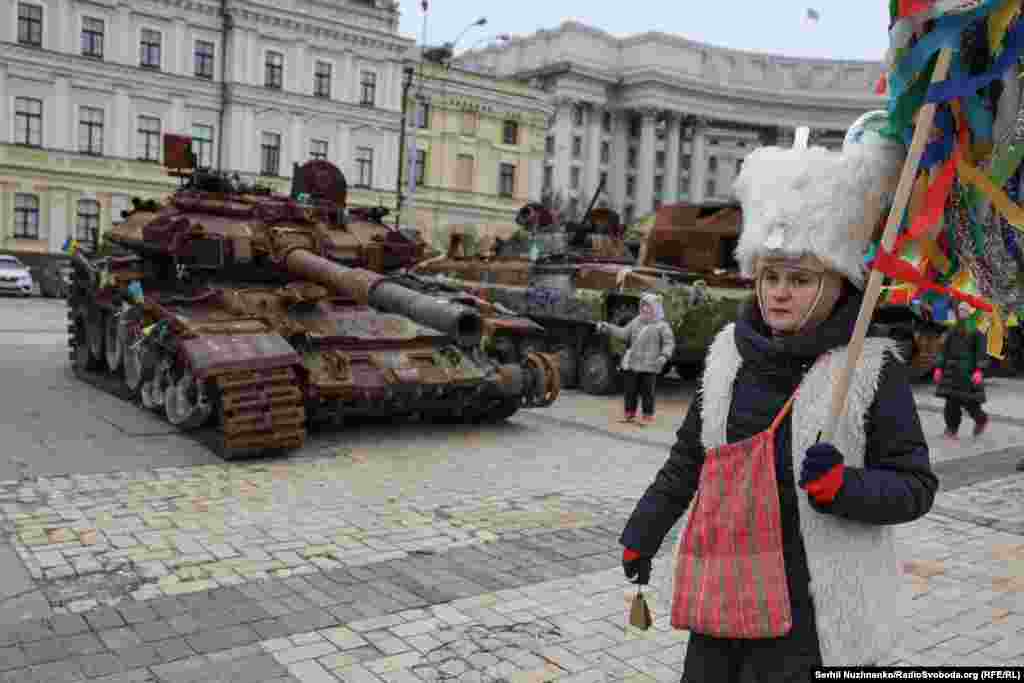 Колядниця на тлі спалених російських танків, які стоять у центрі Києва