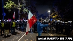 Мужчина с государственным флагом Польши перед полицейским оцеплением. Варшава, 31 октября 2026 года