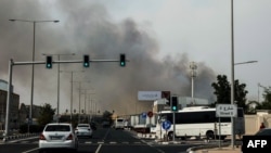 Mașini trec pe lângă un nor de fum care se ridică după un atac iranian în districtul industrial din Doha, pe 1 martie 2026.
