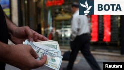 Një tregtar valutash mban kartëmonedha 100 dollarëshe në një kohë kur vlera e rialit iranian ka rënë, Teheran, Iran, 2 maj.