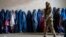 A Taliban fighter stands guard as women wait to receive food rations distributed by a humanitarian aid group in Kabul in May 2023. (file photo)