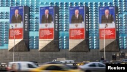 Cars drive past electronic screens on the facade of a building showing an image of Russian President Vladimir Putin in Moscow on February 29.