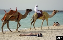 Дубайдағы жағажайда демалып жатқан шетелдік туристердің қасынан өтіп бара жатқан түйе мінген адам. Көрнекі сурет.