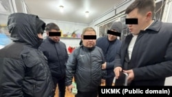 Колунда акча кармап турган шектүү жана УКМКнын кызматкерлери.