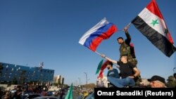 Сирийцы размахивают сирийскими и российскими флагами, протестуя против ракетных ударов США и их союзников. Дамаск, 14 апреля 2018 г.