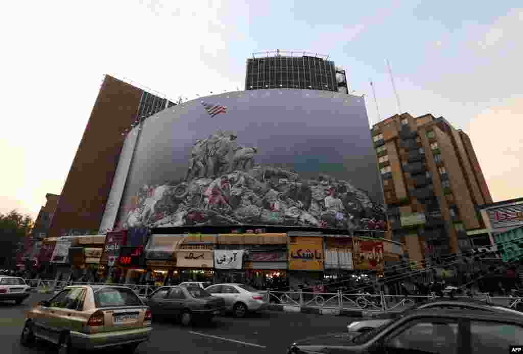 Iranians drive past an anti-U.S. banner inspired by American photographer Joe Rosenthal&#39;s iconic World War II photograph &quot;Raising the Flag on Iwo Jima&quot; in Tehran on November 6. (AFP/Atta Kenare)