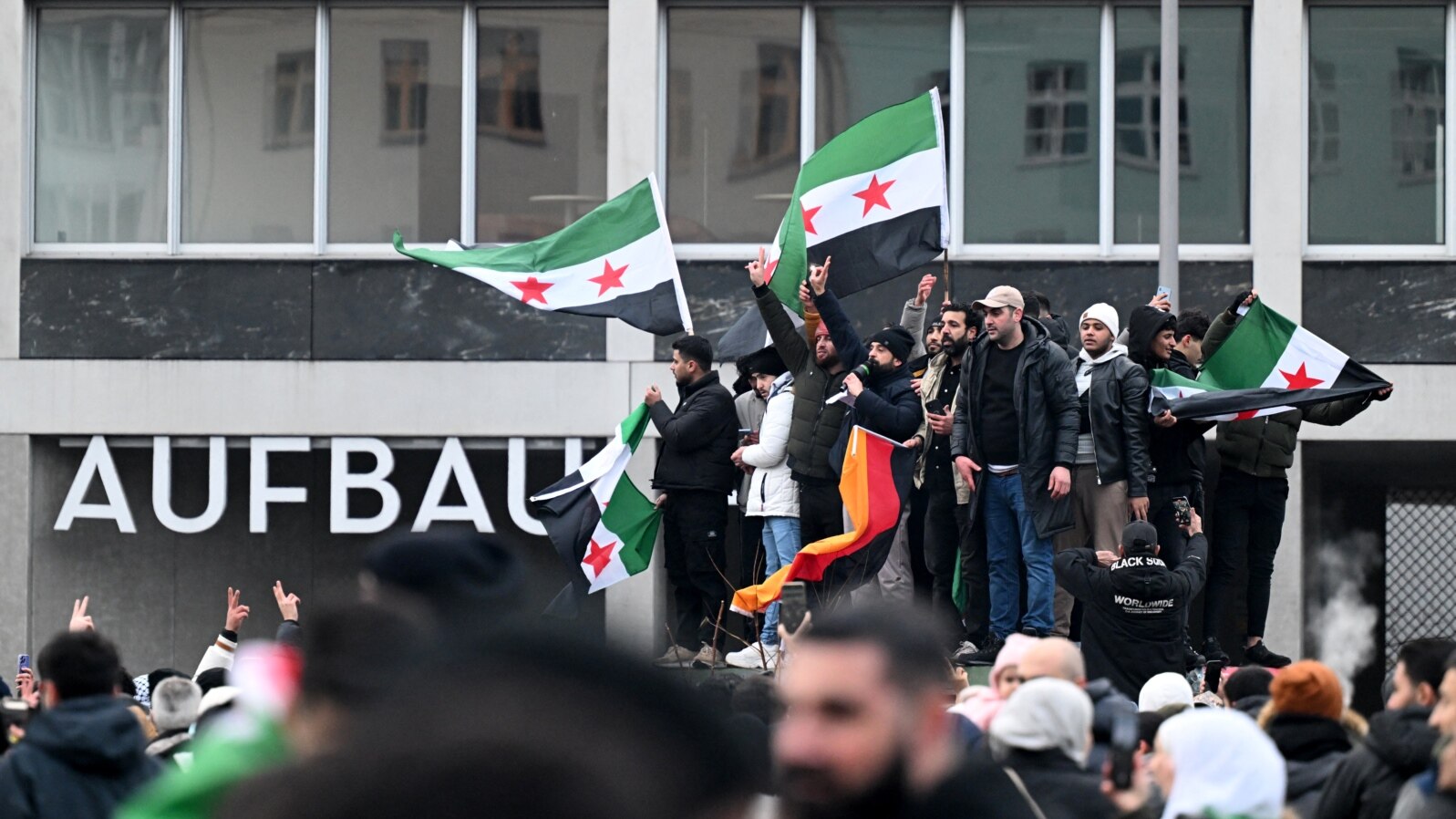 Mai mulți bărbați flutură steaguri siriene și germane în timpul unei manifestații de pe 8 decembrie, la Berlin, pentru a sărbători sfârșitul regimului lui Bashar al-Assad.
