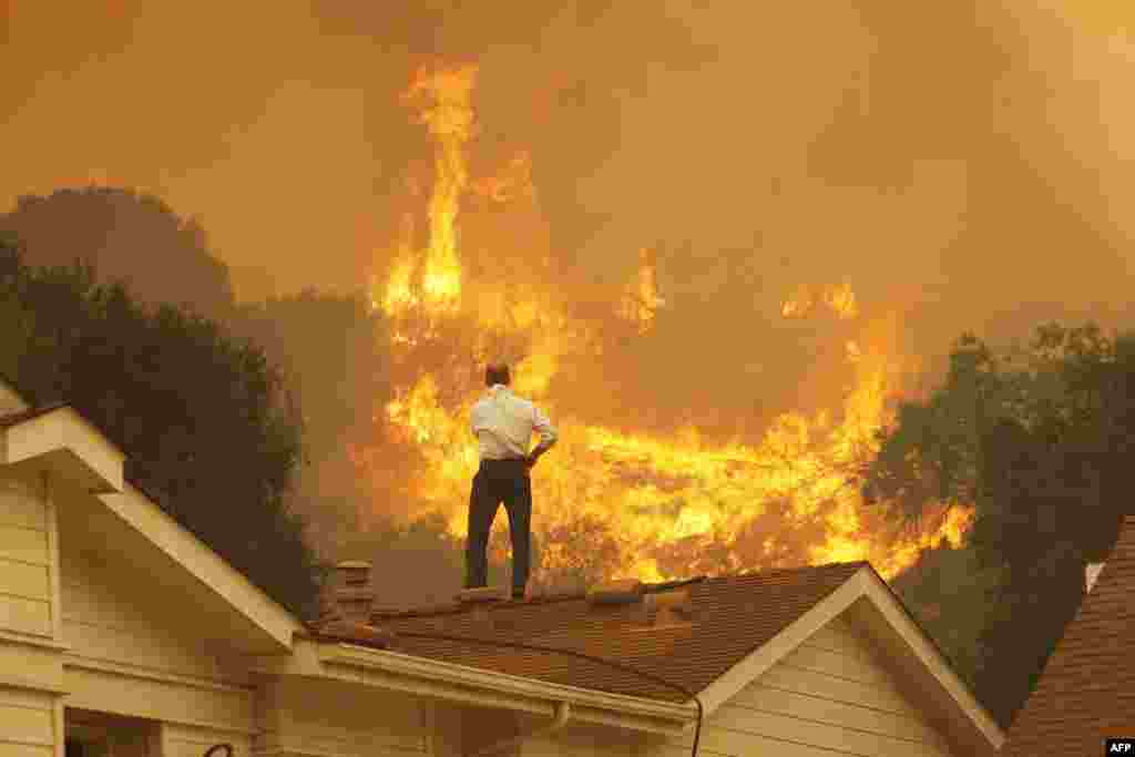 A man on a rooftop looks at the approaching flames of a massive wildfire near Camarillo, California. (Getty Images/David McNew)