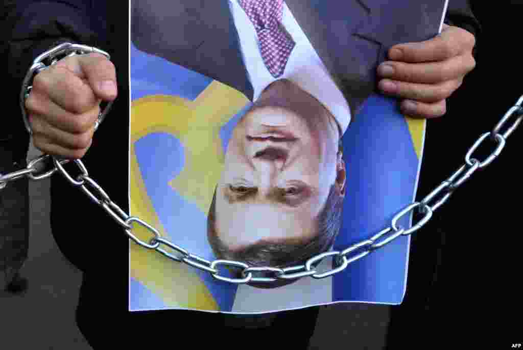 One in a group of protesters holding photos of President Viktor Yanukovych labeled &quot;upside-down&quot; -- which in Ukrainian can carry revolutionary connotations -- during a protest at the Interior Ministry in Kyiv over a brutal attack on journalist Tetyana Chornovol. (AFP/Sergei Supinsky)