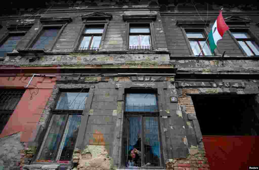 A woman peers out a window of a dilapidated building that shows bullet marks from the 1956 anticommunist uprising, with the revolutionary flag posted on the front, insignia removed, in Budapest. (Reuters/Laszlo Balogh&nbsp;)